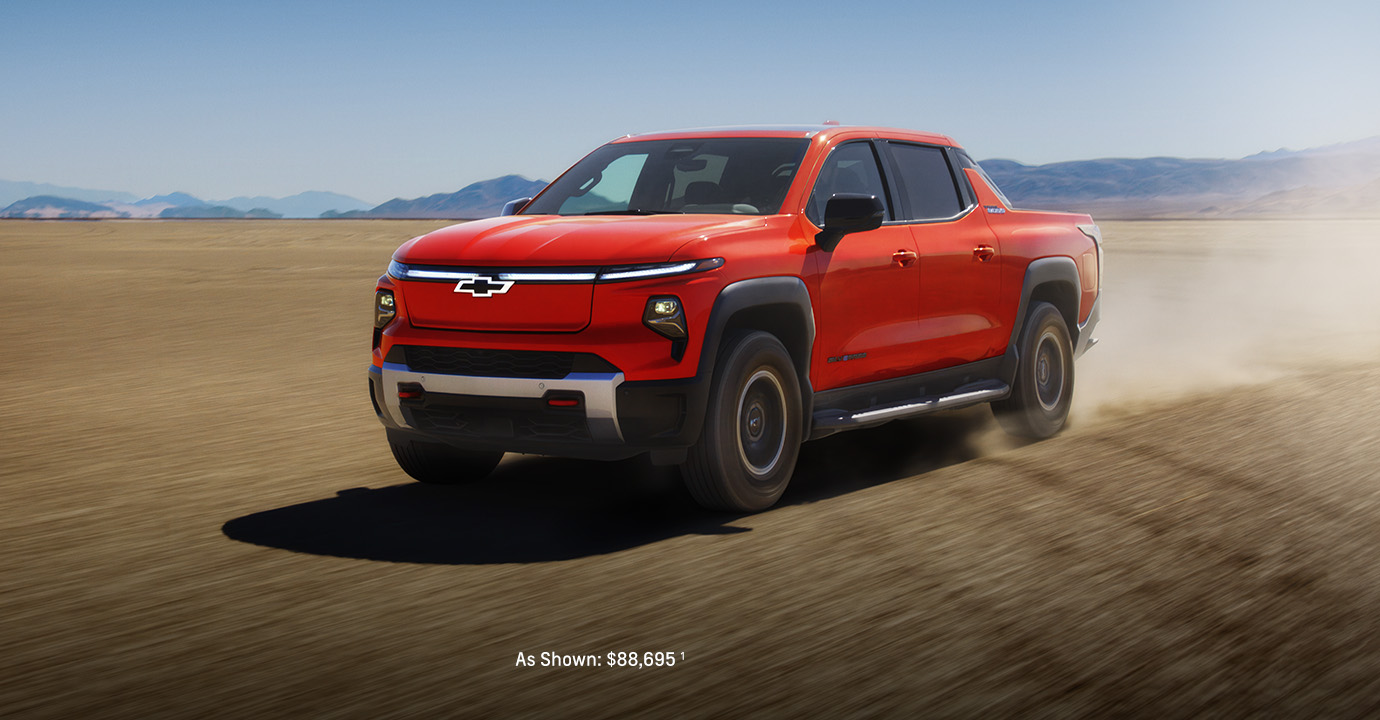 2026 Chevrolet Silverado EV in red driving across an open desert landscape and rugged pickup stance kicking up dust.